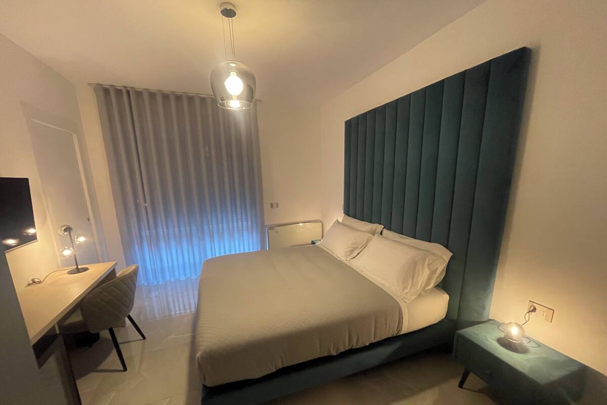 Un dormitorio moderno con cama, mesita de noche, escritorio y lámpara colgante.