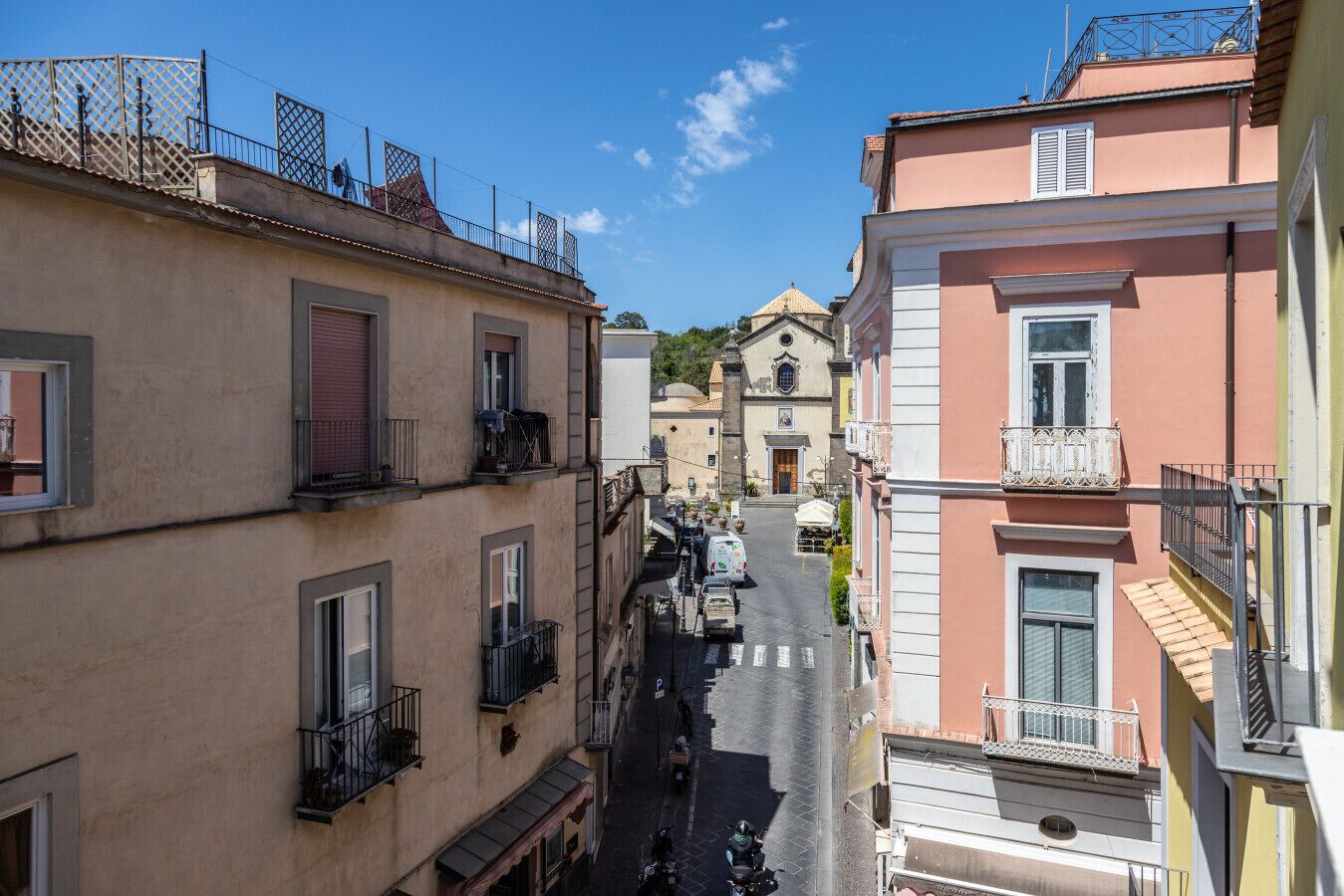 Une rue étroite, bordée de bâtiments des deux côtés, avec une église visible au loin et une moto garée.
