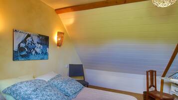 Een slaapkamer met een bed, een stoel, een bureau, een lamp en een schilderij aan de muur.