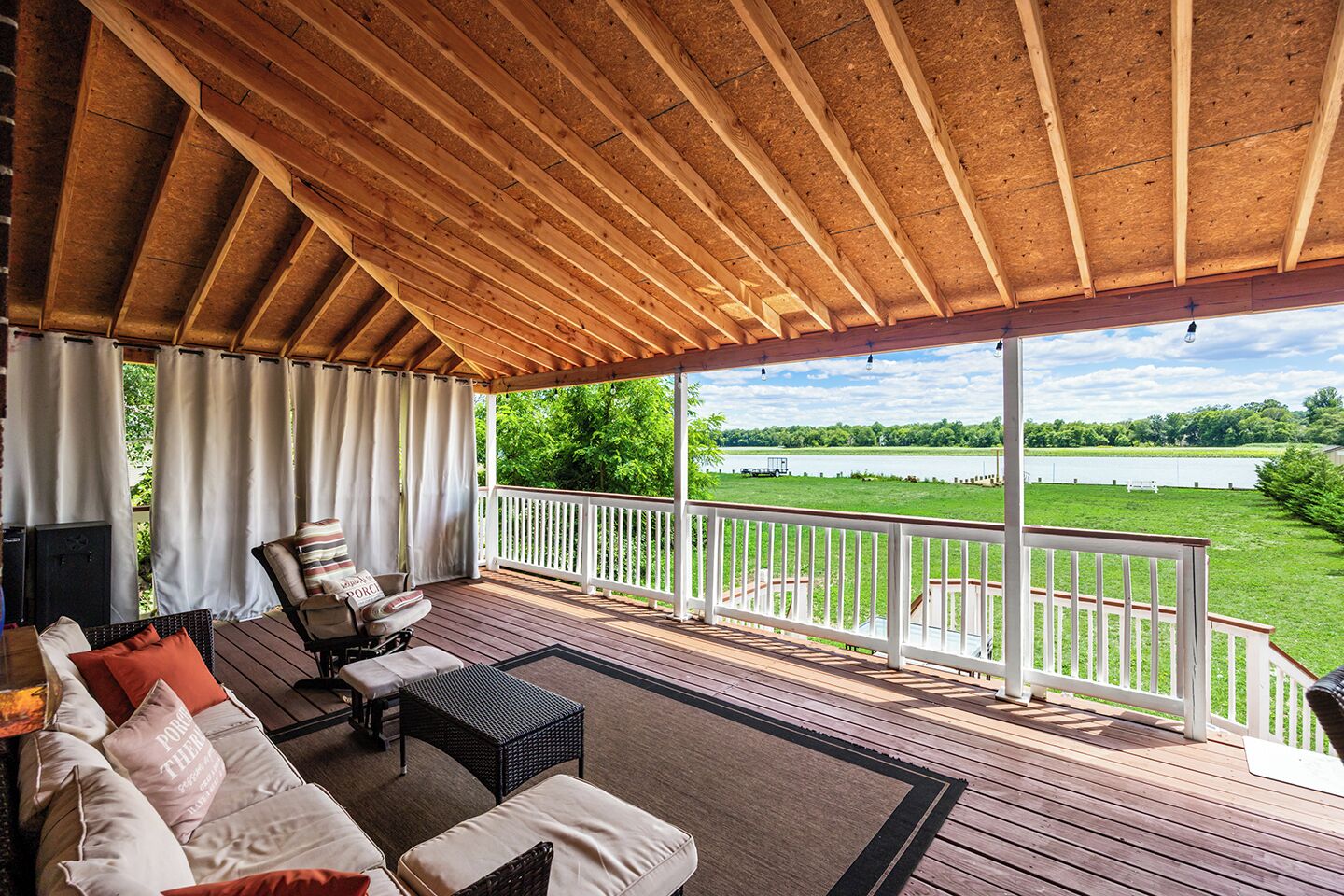 Une véranda avec vue sur un lac, des meubles en bois et une balustrade blanche.