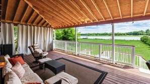 Une véranda avec vue sur un lac, des meubles en bois et une balustrade blanche.