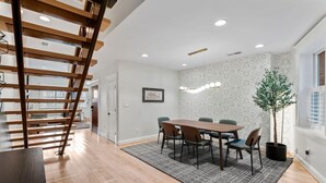 A modern dining area with a wooden table, chairs, a staircase, and a potted plant.