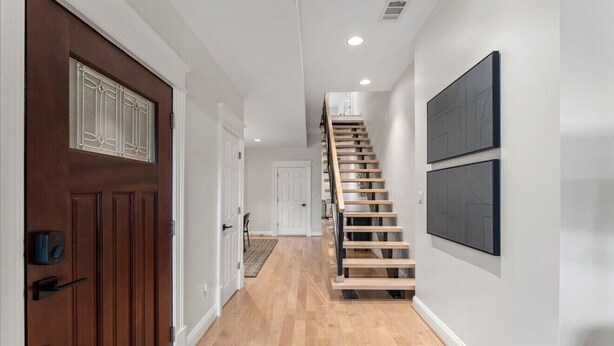 A hallway with a wooden staircase, a door with a window, and a wall-mounted artwork.