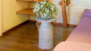 Un coin avec un plancher en bois, une petite table blanche sur pied ornée d’une plante, un canapé violet et une étagère en bois.
