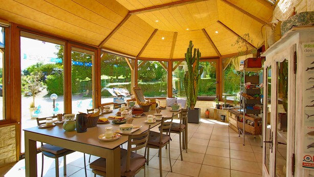 Un espace repas doté d’un plafond en bois, de grandes fenêtres et d’un cactus.