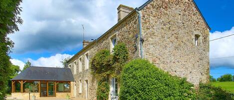 Un bâtiment en pierre doté d’une grande fenêtre et d’une porte, entouré de verdure.