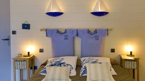 A double bed with matching pillows, two bedside tables with lamps, and a wall-mounted shelf with a small item. - Guest Room 'Chambre Mer' with Shared Terrace, Communal Garden and Wi-Fi (Teurthéville-Bocage)