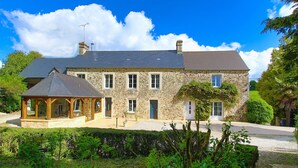 A stone house with a covered porch, a chimney, and a well-maintained garden. - Guest Room 'Chambre Mer' with Shared Terrace, Communal Garden and Wi-Fi (Teurthéville-Bocage)