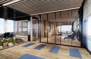 Um espaço interno com piso de madeira, equipamentos de exercícios e uma divisória de vidro.