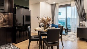 A modern kitchen with dark cabinetry, a built-in refrigerator, and a dining area with a round table set for four. - Cozy Riverside Apartment- Lumiere Skyway (Ho Chi Minh City)