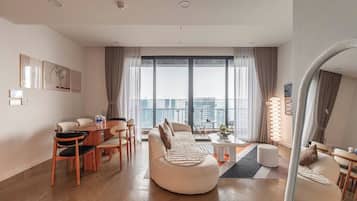A modern living room with a sofa, dining table, chairs, and a large window with a city view.