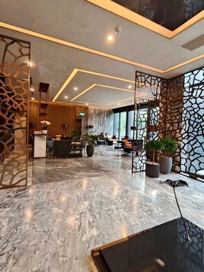 A modern hotel lobby with a marble floor, wooden reception desk, seating area, and decorative screens. - Cozy Riverside Apartment- Lumiere Skyway (Ho Chi Minh City)