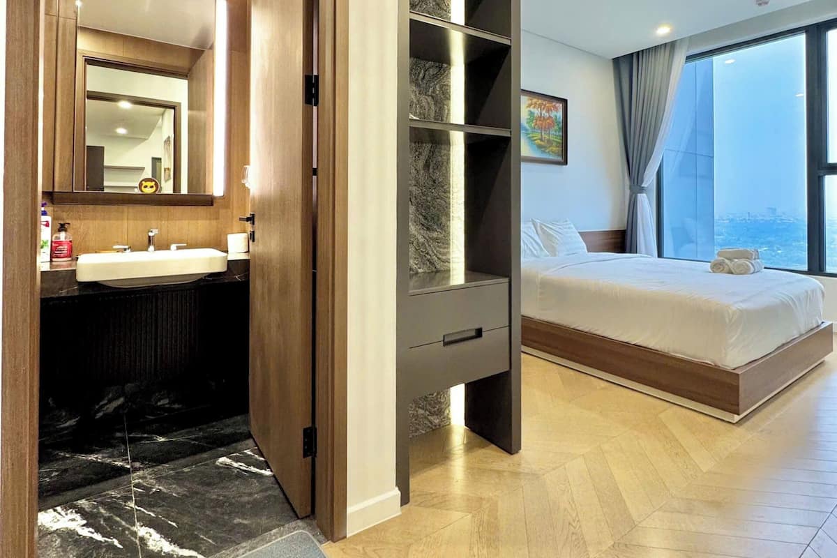 Quarto de hotel moderno com uma cama grande, um closet espaçoso, um banheiro com toucador e vista para a cidade.