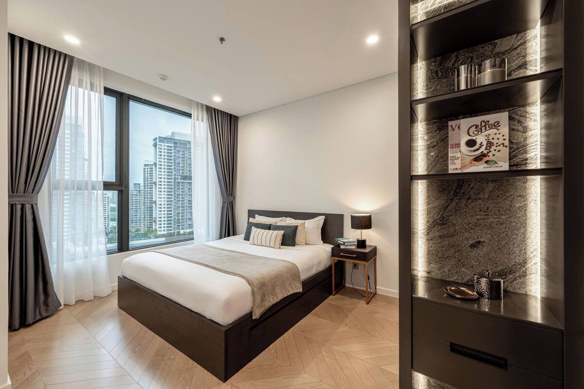 Quarto de hotel moderno com uma cama grande, mesa de cabeceira, espaço para café e vista para a cidade.