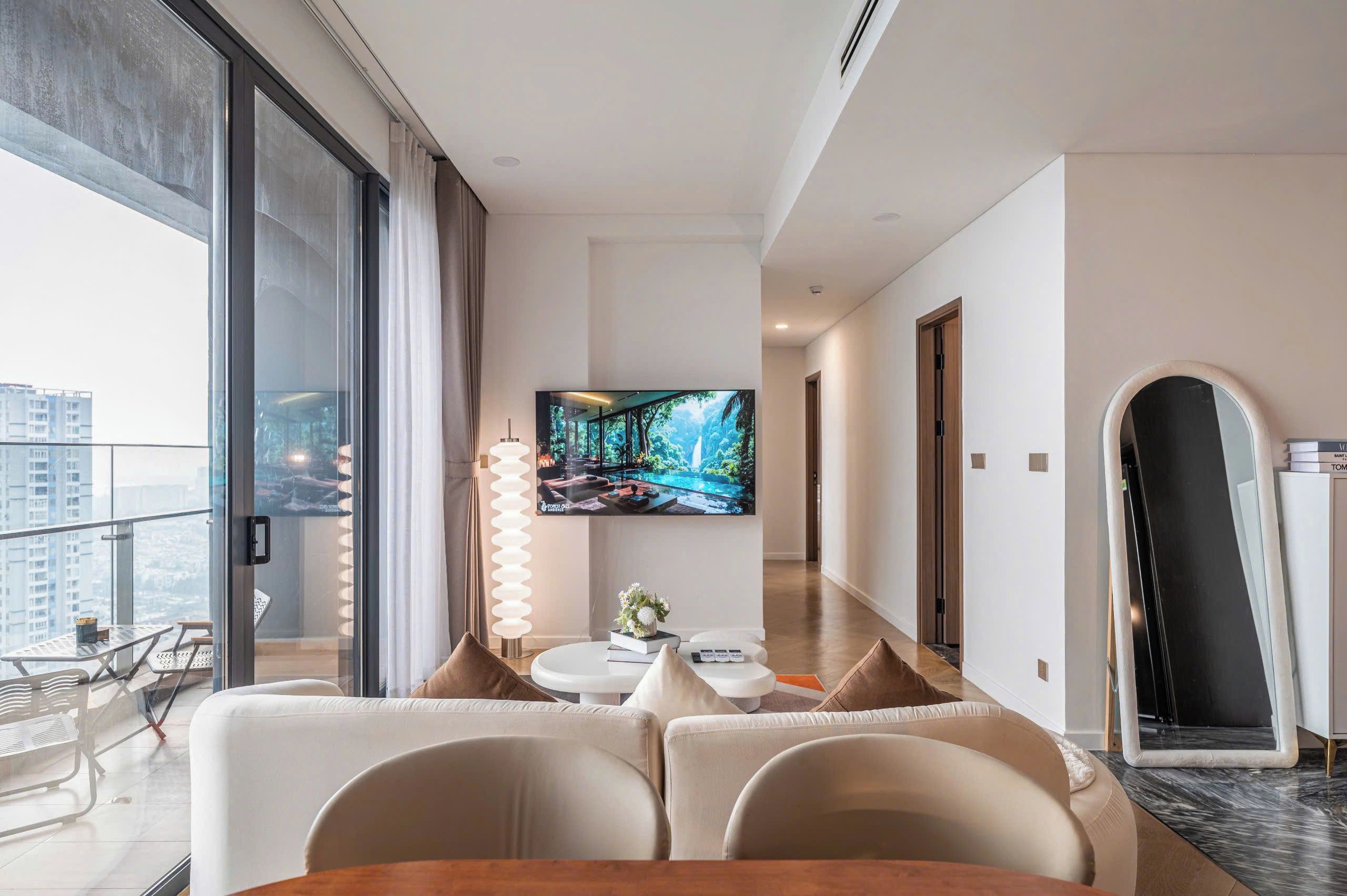 Habitación de hotel moderna con un televisor grande, un sofá, una mesa de comedor y vistas a la ciudad a través de amplias ventanas.