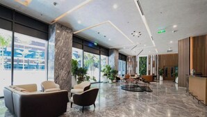 A modern lobby with marble flooring, leather seating, large windows, and indoor plants. - Cozy Riverside Apartment- Lumiere Skyway (Ho Chi Minh City)