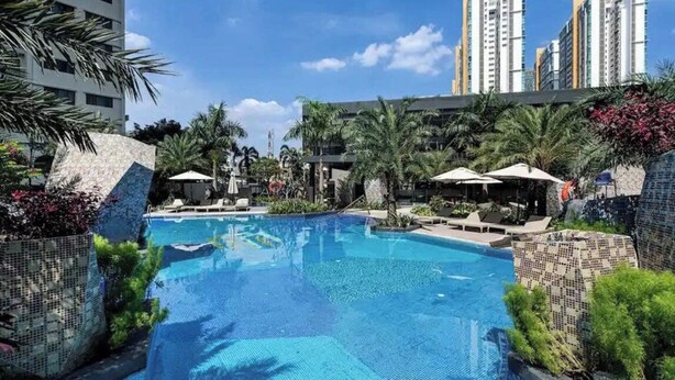 A swimming pool with lounge chairs and umbrellas, surrounded by palm trees and modern buildings. - Cozy Riverside Apartment- Lumiere Skyway (Ho Chi Minh City)