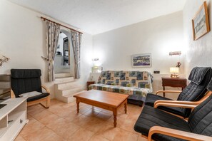 Un soggiorno con un divano, due poltrone, un tavolino in legno, un mobile TV e una finestra con tende.