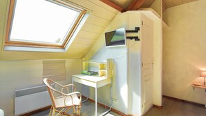 Et værelse med skråvæg, et skrivebord med en computer, en stol, en radiator og et vindue.