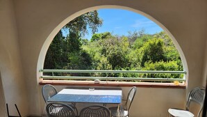 Un balcone all'aperto con tavolo e sedie, vista sul verde e ringhiera.