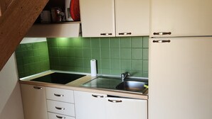 Una cucina con una scala in legno, zoccolo a parete in piastrelle verdi e mobili bianchi.