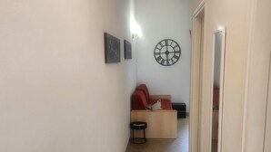 Un corridoio stretto con pavimento piastrellato, un divano rosso, un piccolo tavolino rotondo e un orologio a parete.