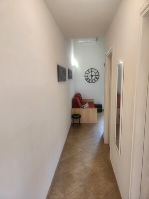 Ein schmaler Flur mit Fliesenboden, einem roten Sofa, einem kleinen runden Tisch und einer Wanduhr.
