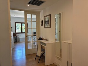 Ein Zimmer mit Schreibtisch, Stuhl, Fenster und einer Tür zu einem anderen Raum.