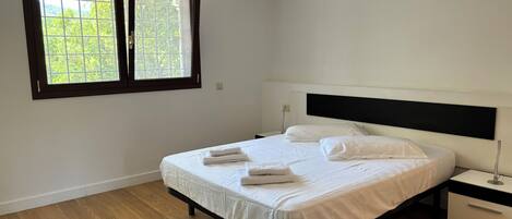 A bedroom with a bed, a nightstand, a window, and a wooden floor.