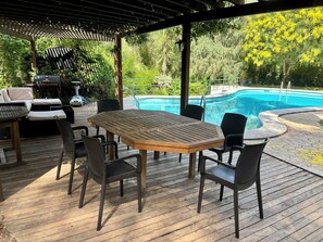 Eine Holzterrasse mit Tisch und Stühlen, einem Pool und einer überdachten Sitzgruppe.
