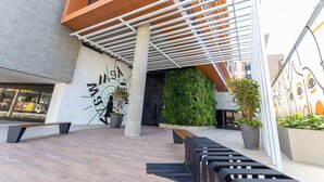 An outdoor seating area with benches and planters, a wall with a clock, and a modern architectural design. - Way Tambau #R4 - Style and Comfort By Carpediem (João Pessoa)