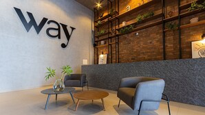 A modern lobby with a large 'way' sign, a brick wall with shelves, and two grey armchairs. - Way Tambau #R4 - Style and Comfort By Carpediem (João Pessoa)