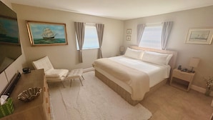 A bedroom with a bed, a chair, a nightstand, a lamp, a painting, and a window with curtains. - Modern romantic escape designed for comfort. (Jensen Beach)