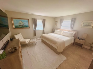 A bedroom with a bed, a chair, a nightstand, a lamp, a painting, and a window with curtains. - Modern romantic escape designed for comfort. (Jensen Beach)