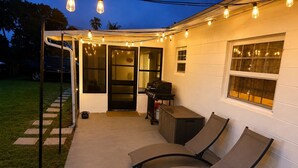 An outdoor patio with a grill, a covered seating area, and string lights. - Modern romantic escape designed for comfort. (Jensen Beach)