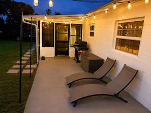 An outdoor patio with a grill, a covered seating area, and string lights. - Modern romantic escape designed for comfort. (Jensen Beach)