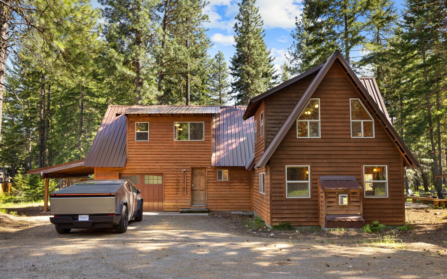 A two-story wooden cabin with a garage, surrounded by a forest.