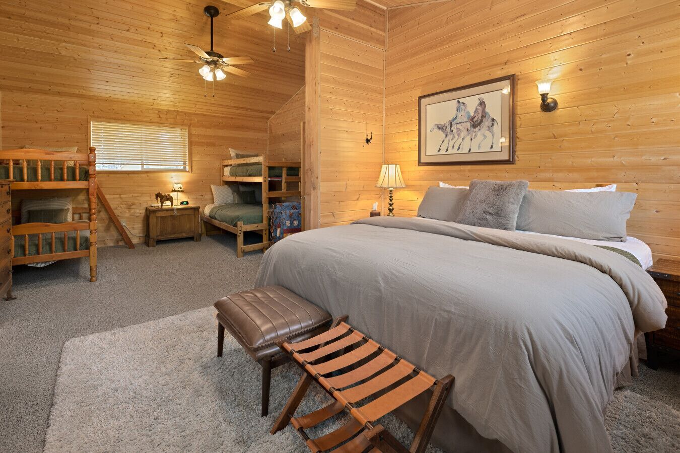 A wooden cabin bedroom with bunk beds, a bed, a desk, and a chair.