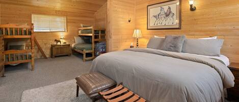 A wooden cabin bedroom with bunk beds, a bed, a desk, and a chair.