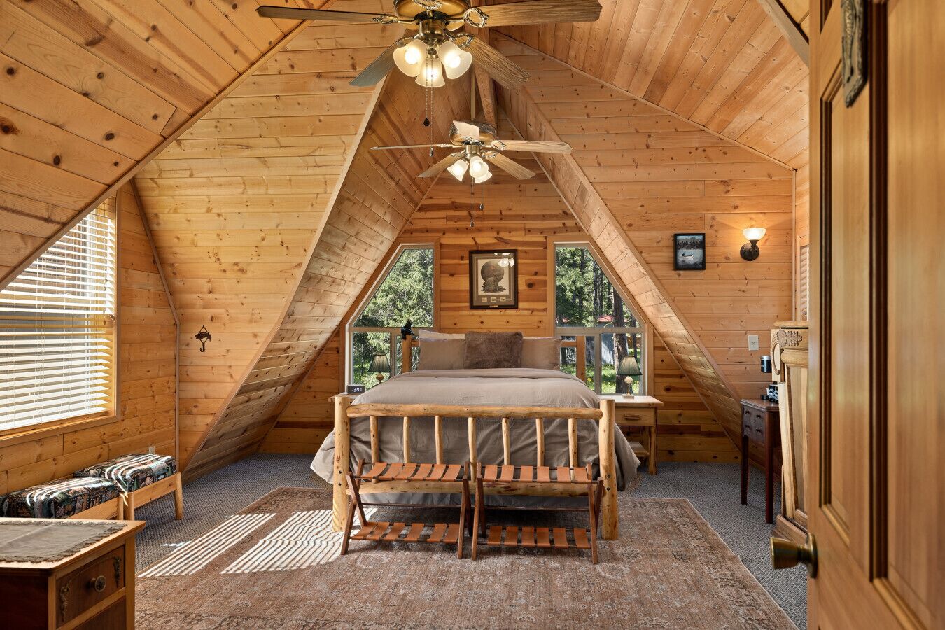 Un dormitorio acogedor en el ático, con una cama, un banco de madera, un ventilador de techo y una ventana con persianas.