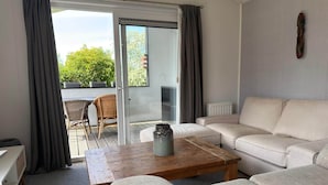 Sala de estar com sofá, mesa de madeira e porta de vidro deslizante que dá para área externa com mesa e cadeiras.