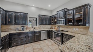 Una cocina moderna con armarios oscuros, encimeras de granito, electrodomésticos de acero inoxidable y suelo de baldosas.