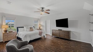 Un dormitorio con cama, televisión, ventilador de techo, cómoda y ventana.