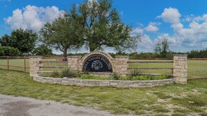 Un arco de piedra con la inscripción 'HILL VALLEY ESTATES' y un área ajardinada con césped y árboles.