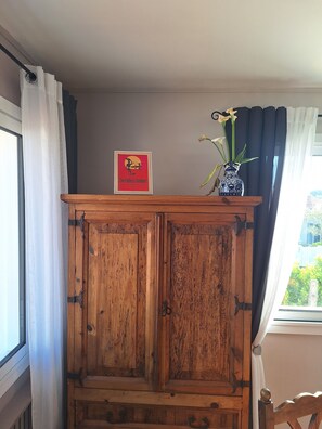A wooden cabinet with a framed poster, a vase with flowers, and a window with curtains. - L'Horizon - Endless Summer (4 pers) (La Tranche-sur-Mer)