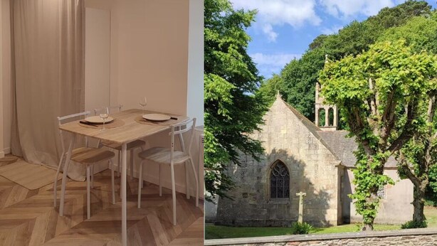 Un comedor con mesa y sillas de madera, un edificio de piedra con ventana, y abundante vegetación.