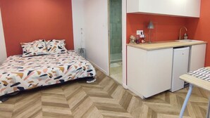 Un dormitorio con cama, un kitchenette pequeño y un baño con puerta de vidrio.