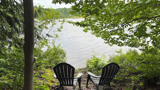 Deux fauteuils Adirondack sont placés face à un lac, entourés d’arbres et de feuillage.