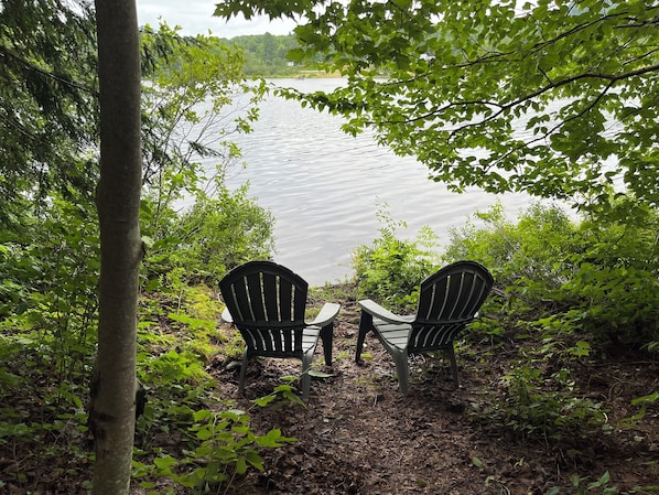 Deux fauteuils Adirondack sont placés face à un lac, entourés d’arbres et de feuillage.