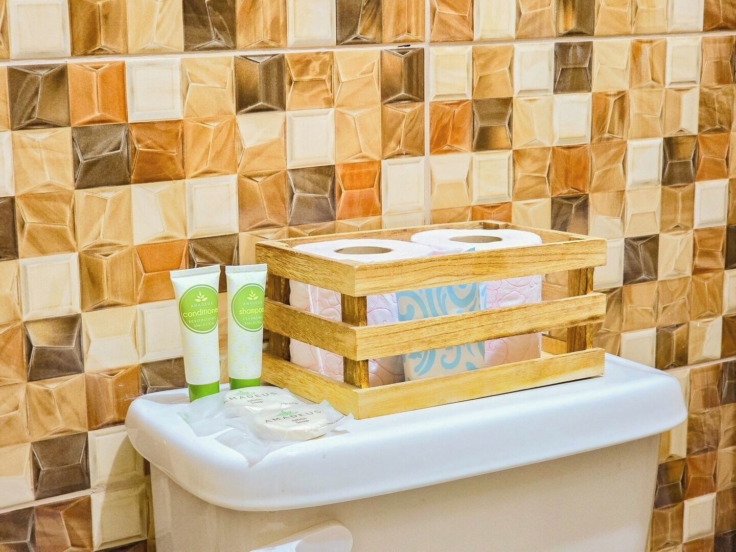 A toilet with a wooden tissue holder, two tubes of shampoo, and toilet paper.